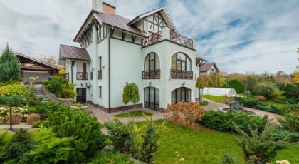 Beautiful villa surrounded by lush gardens and fountains, under a cloudy sky.