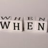 Minimalist photo of wooden blocks with the word 'WHEN' on a white background.