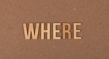 Wooden letters spelling 'WHERE' on a brown cardboard background.