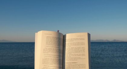 An open book is held by the ocean under the calming sunset sky.
