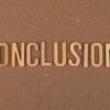 Wooden letters arranged to spell 'Conclusion' on a brown cardboard background.