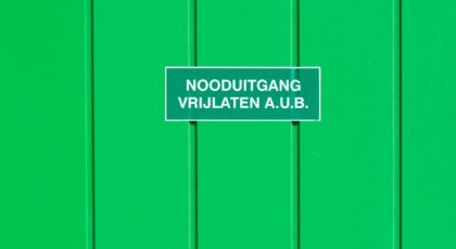 A green metal wall featuring an emergency exit sign in Dutch. Perfect for safety-themed graphics.
