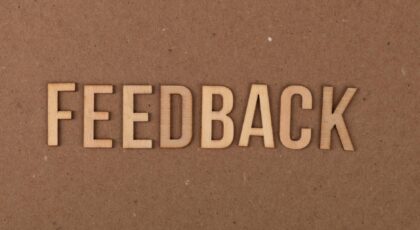 A close-up of a wooden 'FEEDBACK' sign on a textured cardboard background.