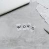 Top view of a workspace with scattered paper letters spelling 'WORD', next to a laptop and scissors.
