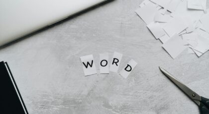 Top view of a workspace with scattered paper letters spelling 'WORD', next to a laptop and scissors.