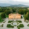A stunning aerial view of a historic villa and gardens in Italy, surrounded by lush greenery.