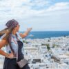 A young woman admires the beautiful seaside town of Mykonos, Greece, under a clear summer sky.