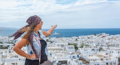 A young woman admires the beautiful seaside town of Mykonos, Greece, under a clear summer sky.