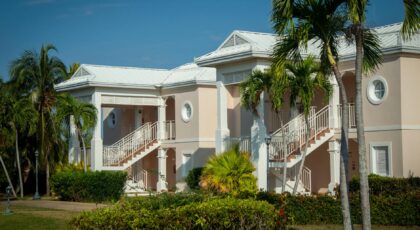 Exterior view of a tropical resort with classic architecture and lush palm trees under a clear blue sky.