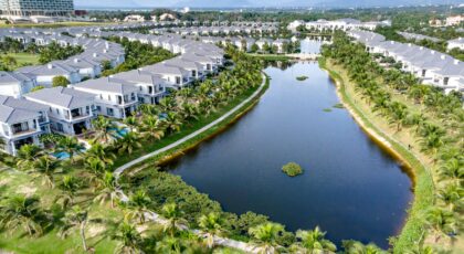 Aerial shot of a tropical resort with villas and a palm-surrounded lake under a clear sky.