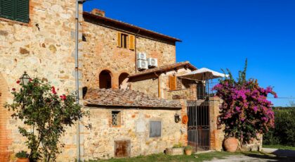 A beautiful rustic villa in Toscana, Italia, showcasing classic stone architecture and vibrant bougainvillea under a clear blue sky.