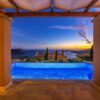 Stunning view of a luxury villa and infinity pool overlooking the sea at sunset.