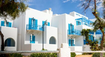 Whitewashed Greek hotel with blue shutters in Naxos under a clear sky.