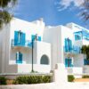 Whitewashed Greek hotel with blue shutters in Naxos under a clear sky.
