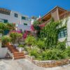 Mediterranean villa adorned with lush greenery and vibrant flowers, under a clear blue sky.