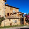 A beautiful rustic villa in Toscana, Italia, showcasing classic stone architecture and vibrant bougainvillea under a clear blue sky.