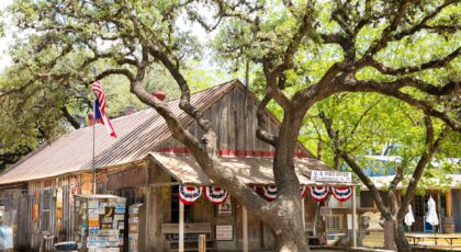 Rustic wooden post office in Luckenbach, Texas, with American flag and oak tree.