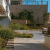 A sunny Mediterranean courtyard featuring rustic stone walls and wooden seating.