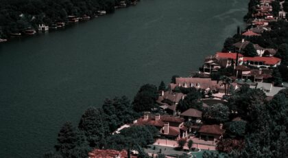 Aerial view of elegant homes along a tranquil river surrounded by lush greenery, showcasing affluence and scenic beauty.