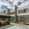 Stylish modern villas with wooden accents and thatched roofing by a pool under a vibrant sky in Bahia, Brazil.